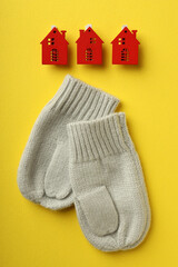 Concept of heating season with mittens and red houses on yellow background