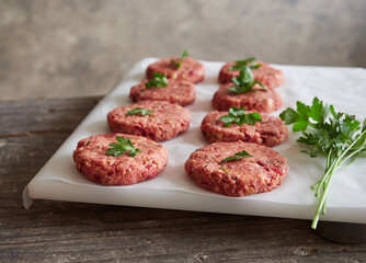 rows of freshly prepared homemade raw vegan burger patties placed on white parchment paper with parsley on top. Meat alternative.