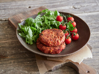 homemade veggie burgers served with rocket and cherry tomatoes on a dark rustic plate on a wooden table