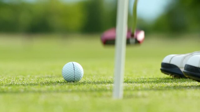 Close-up of a golfer putting his golf ball on the grass and hitting the golf ball with one shot. The golf ball is shot in the direction of the camera and holed.