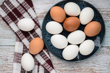 Raw chicken white and brown eggs in a plate on a wooden background. Cooking concept. Easter holiday. Selective focus. Top view, flat lay.