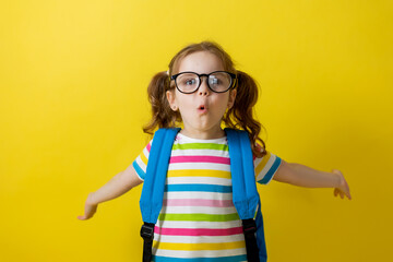 portrait of a girl with glasses and a striped T-shirt with a school backpack on a yellow background. joyful child is in a hurry to go to school. concept of education. photo studio, space for text. 