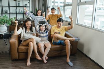 Portrait of happy Multi-generational Asian family in living room at home. Portrait of extended family group sitting together and using mobile phone, laptop, digital tablet and vr. - Powered by Adobe