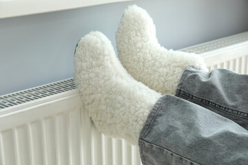 Concept of heating season with legs in knitted boots on radiator