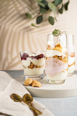 Three glasses with a layered creamy yoghurt dessert trifle with cookies, amaretti, cherries and thyme in a tropical setting