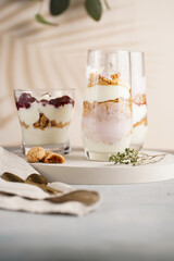 Three glasses with a layered creamy yoghurt dessert trifle with cookies, amaretti, cherries and thyme in a tropical setting