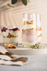 Three glasses with a layered creamy yoghurt dessert trifle with cookies, amaretti, cherries and thyme in a tropical setting