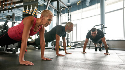 Strong senior couple doing plank at gym