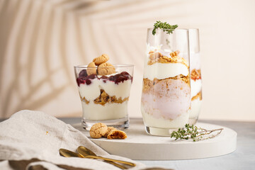 Three glasses with a layered creamy yoghurt dessert trifle with cookies, amaretti, cherries and thyme in a tropical setting