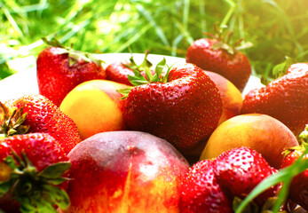 Strawberries and peaches on a plate on the green grass. Delicious and fresh summer fruits. Healthy vegetarian food with vitamins.
