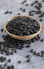 Fototapeta na wymiar Ceramic bowl full of dry black beans on grey table closeup