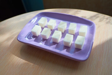 A purple plate with ten pieces of white sugar stands on a table under the sun.