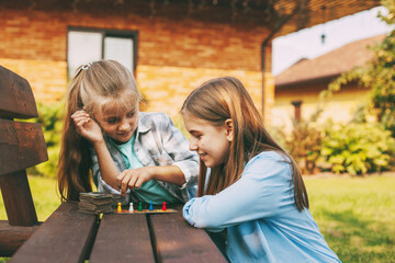 Two sisters laugh and play a wooden board game with colorful blue, red, green and yellow chips...