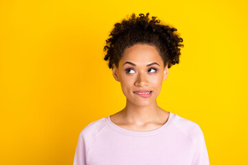 Photo of young dark skin curious woman look empty space minded bite teeth lips isolated on yellow...
