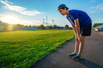 teen boy boy does physical exercises at the stadium track, a soccer field with green grass - concept of sports and health