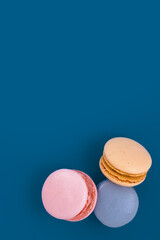 Orange, pink and blue macarons against a mykonos blue background with copy space. Almond French macaroon cookies. Top view