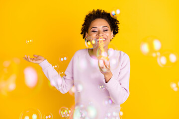 Photo of young happy dark skin woman blow air bubbles smile good mood isolated on yellow color...