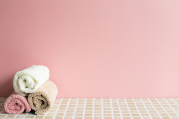 Obraz na płótnie Canvas Bathroom towel on mosaic tile table. pink wall background. Skin care and spa concept. Home interior
