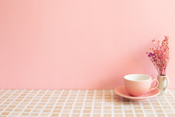Coffee cup and vase of dry flowers on mosaic tile table. pink wall background. Home interior