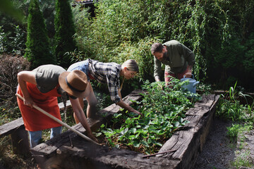 Happy young and old farmers working with garden tools outdoors at community farm.