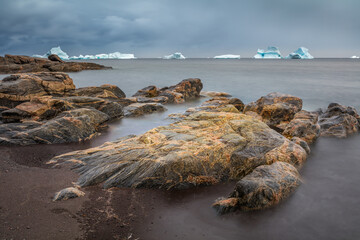 Long exposure image of a seascape with rocks and icebergs floating in the sea, Disko Island,...