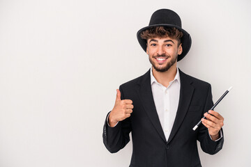 Young arab wizard man holding a wand isolated on white background smiling and raising thumb up