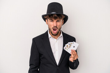Young arab wizard man holding a magic cards isolated on white background screaming very angry and...