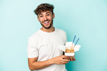 Young arab man holding a take away noodles isolated on blue background laughing and having fun.