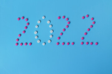 Christmas, New Year flat lay on blue background. numbers 2022 making with pills and medical mask. Top view. Copy space. Mock up. Concept of health care. New normal life after COVID-19. Copy space.