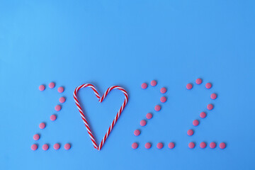 Christmas, New Year, Valentine's Day flat lay on blue background with place for text. numbers 2022 making with pills and heart of sweet candies. Top view. Copy space. Mock up.