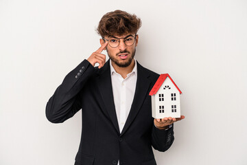 Young arab real estate man holding a model house isolated on isolated background showing a...