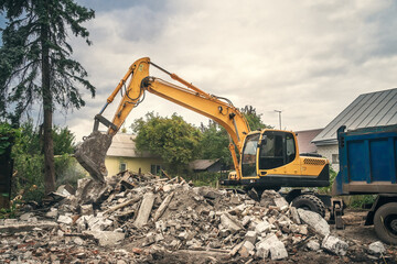 Demolition of building by industrial excavator. Demolished broken walls and roof of old house, pile of industrial garbage.
