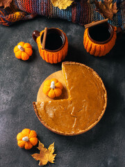 Homemade pumpkin pie on Thanksgiving. Two cups of coffee or tea in a knitted sweater. warm autumn scarf, maple leaves and crocheted pumpkins.