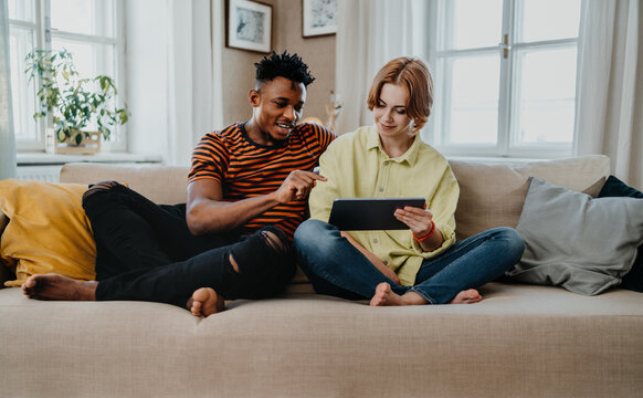 Young biracial couple using tablet, having fun indoors at home, checking social networks together.