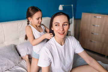 mom and daughter are in bed in the morning, mom is combing her daughter's hair, daughter is combing mom