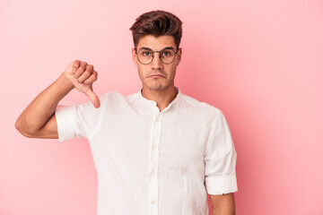 Young caucasian man isolated on pink background showing a dislike gesture, thumbs down....