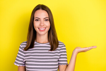 Photo of lovely young brunette lady hold empty space wear striped t-shirt isolated on yellow color...