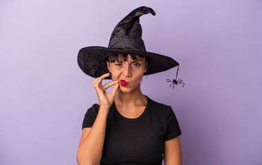 Young mixed race woman disguised as a witch isolated on purple background  with fingers on lips keeping a secret.