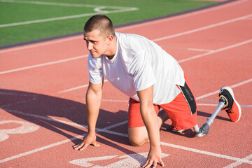 Fototapeta premium Caucasian male athlete with a prosthetic leg standing at the start on the track at the stadium. Sport concept.
