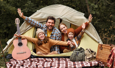 Happy family father, mother and two little children sitting in tent at campsite in forest