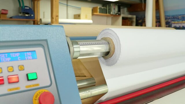 A white roll of fabric rotates on a calender. In the background you can see the transfer paper. The machine runs at 190 degrees Celsius.