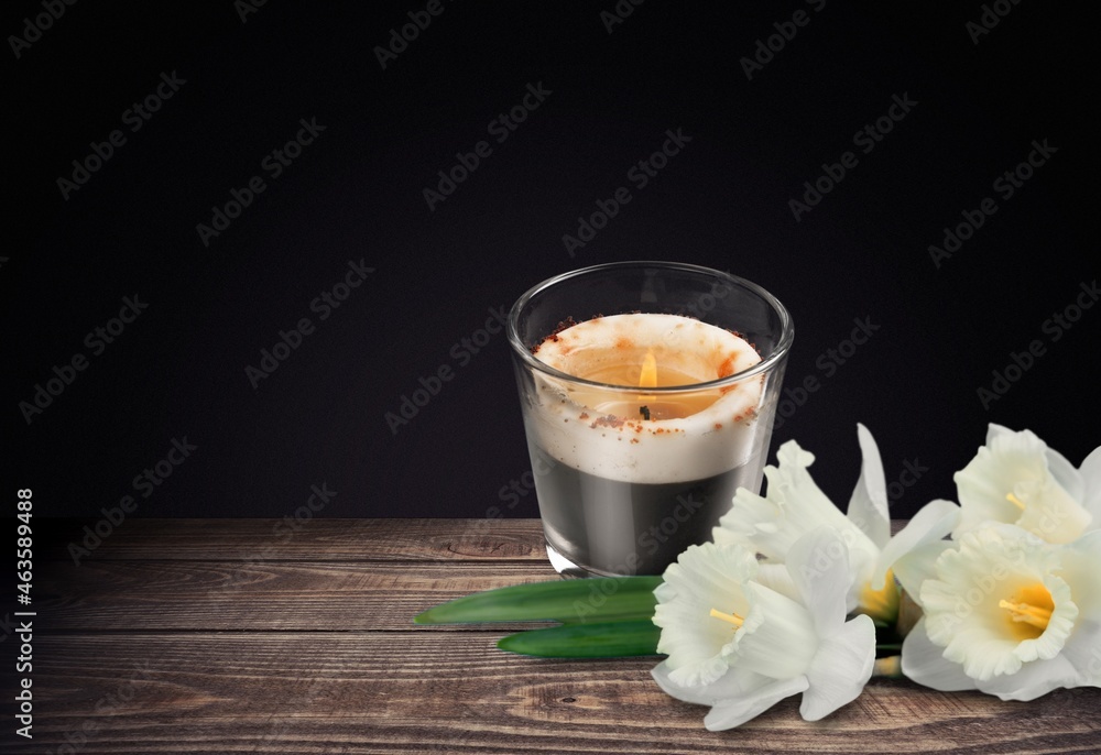 Sticker WHITE FLOWER NEXT TO A LIGHTED CANDLE ON DARK BACKGROUND. DEATH, RELIGIOUS CEREMONY,