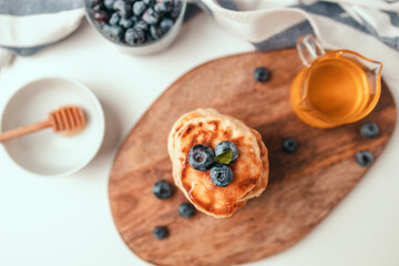 Delicious pancakes with fresh blueberries and honey syrup on a gray table on a light background for a breakfast, copy space. Top view, flat lay