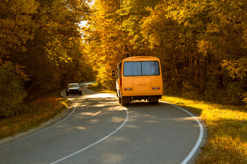 Fototapeta na wymiar Road with school bus in beautiful autumn forest at sunset.