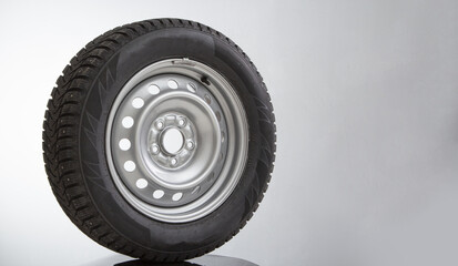 Car wheel and winter studded tire on grey background