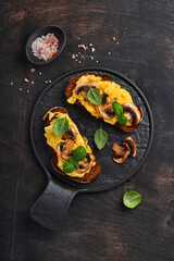 Scrambled eggs with fried mushrooms and basil on bread on black table background. Homemade breakfast or brunch meal - scrambled eggs and mushrooms sandwiches. Top view with copy space