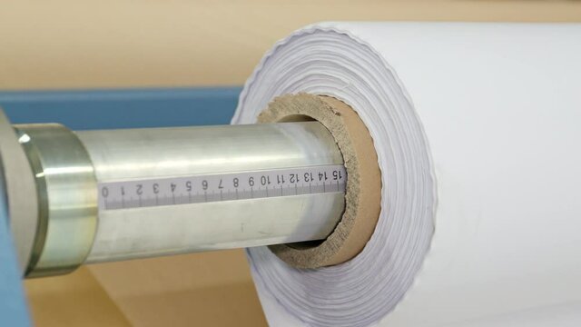 Close-up of a calender turning a roll of white fabric. In the background you can see the transfer paper.