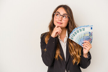 Young caucasian business woman holding banknotes isolated on white background looking sideways with doubtful and skeptical expression.