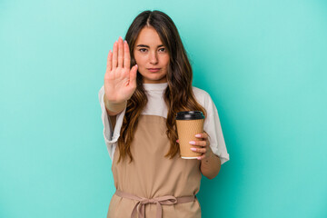 Young caucasian store clerk woman holding a takeaway coffee isolated on blue background standing with outstretched hand showing stop sign, preventing you.