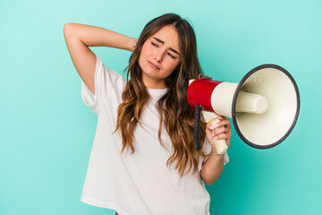 Young caucasian woman holding a megaphone isolated on blue background touching back of head, thinking and making a choice.